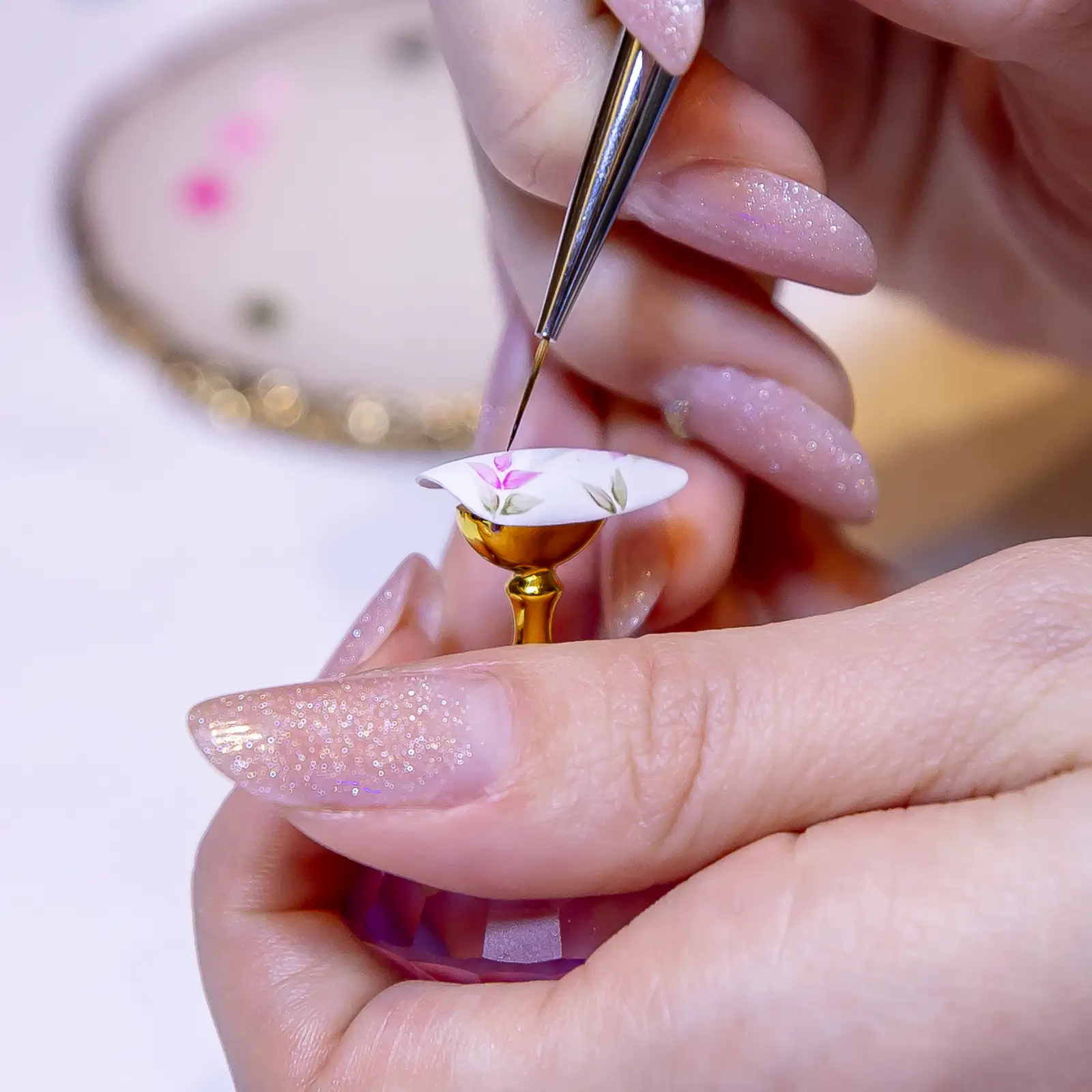 A fine brush painting detail onto a single pale pink fingernail, close up